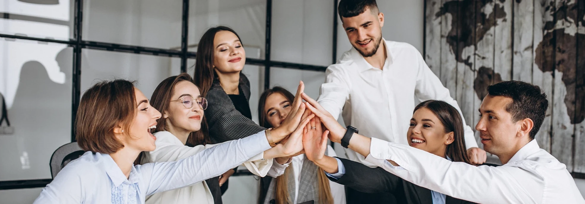 Group of young professionals in business attire celebrating teamwork with a high-five, symbolizing collaboration, growth, and success in the real estate sector.